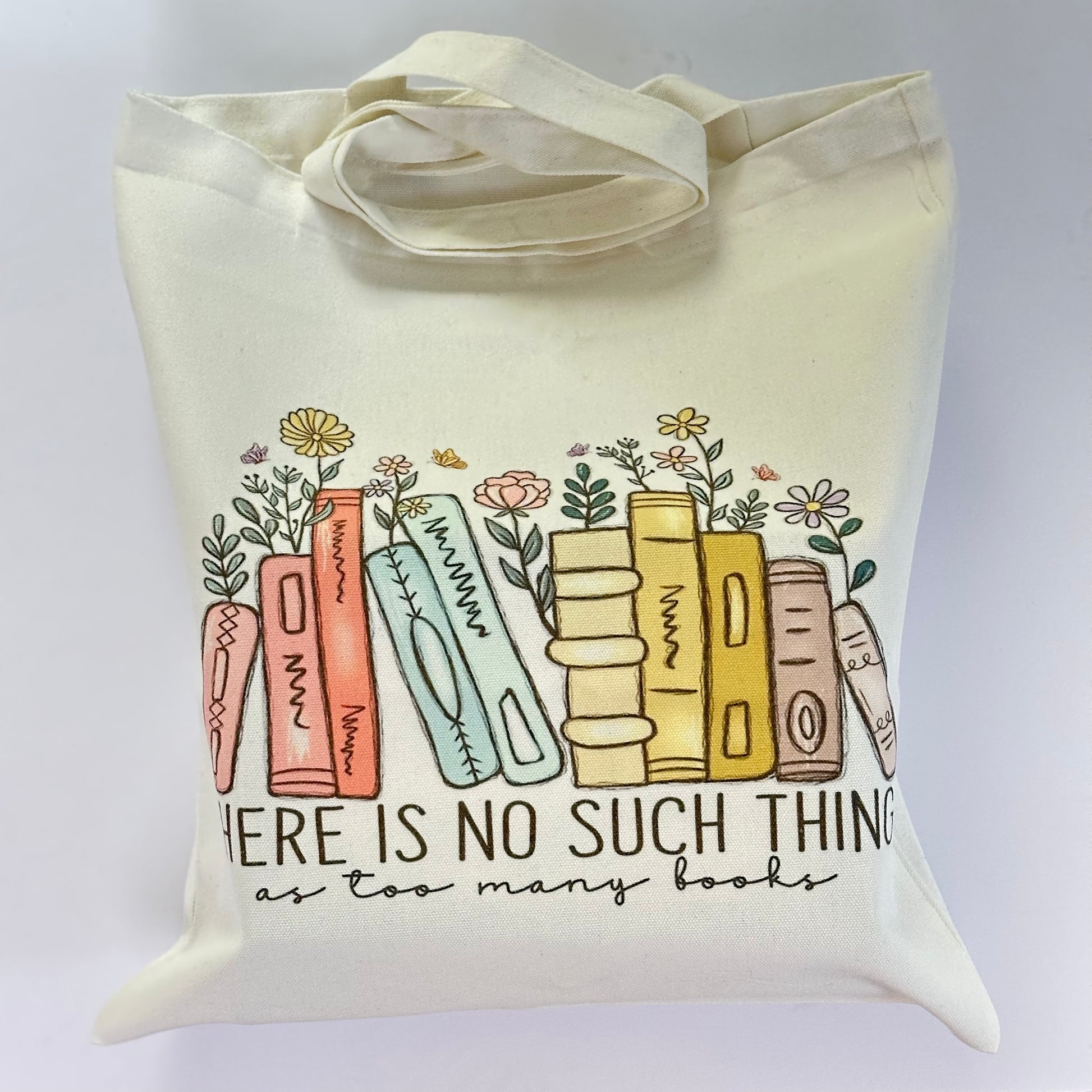 Tote bag with book illustration and text 'Here is no such thing as too many books' on a white background