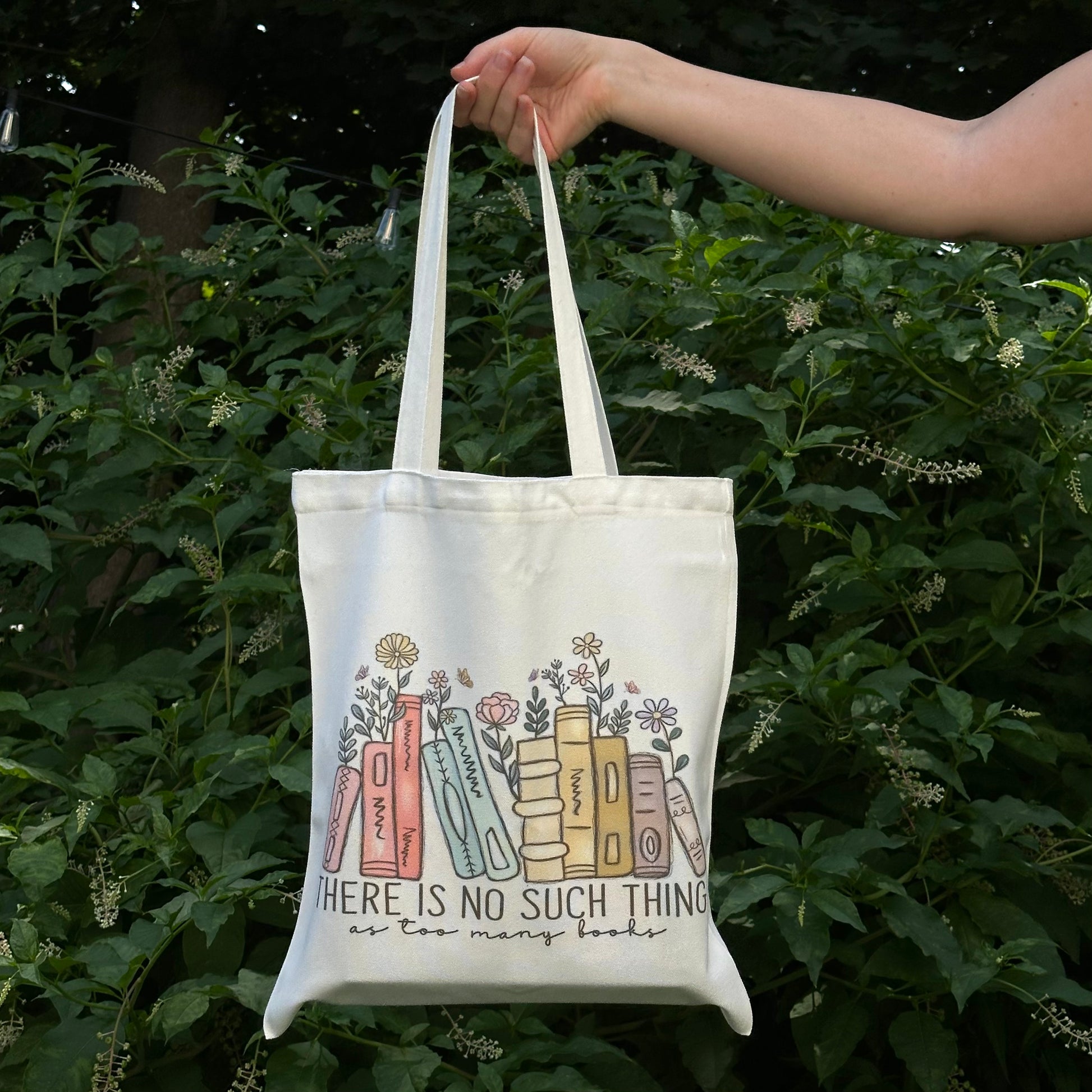 Tote bag with book design and text held by a hand against a green leafy background