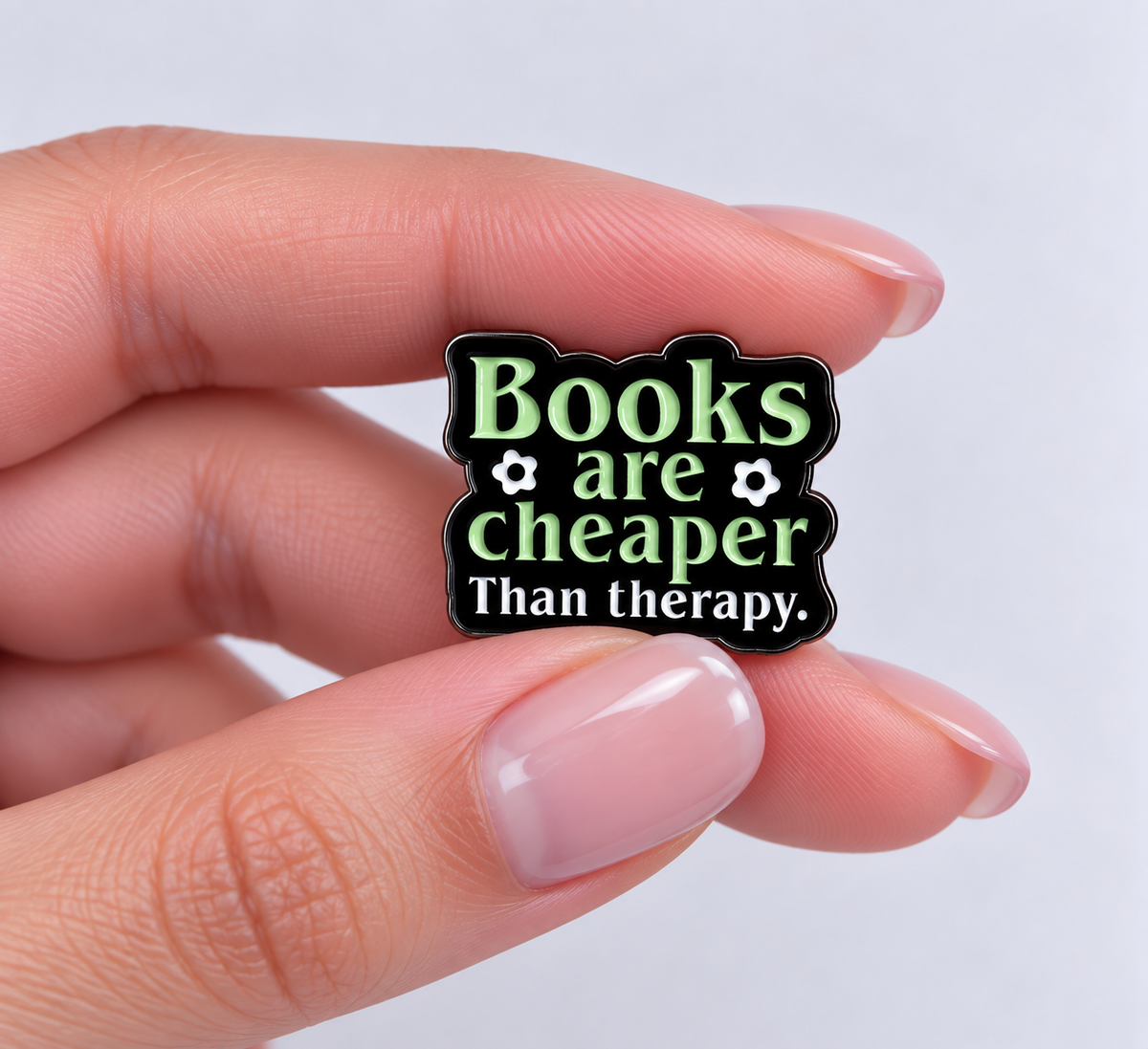 Books Are Cheaper Than Therapy enamel pin held in hand to show its size