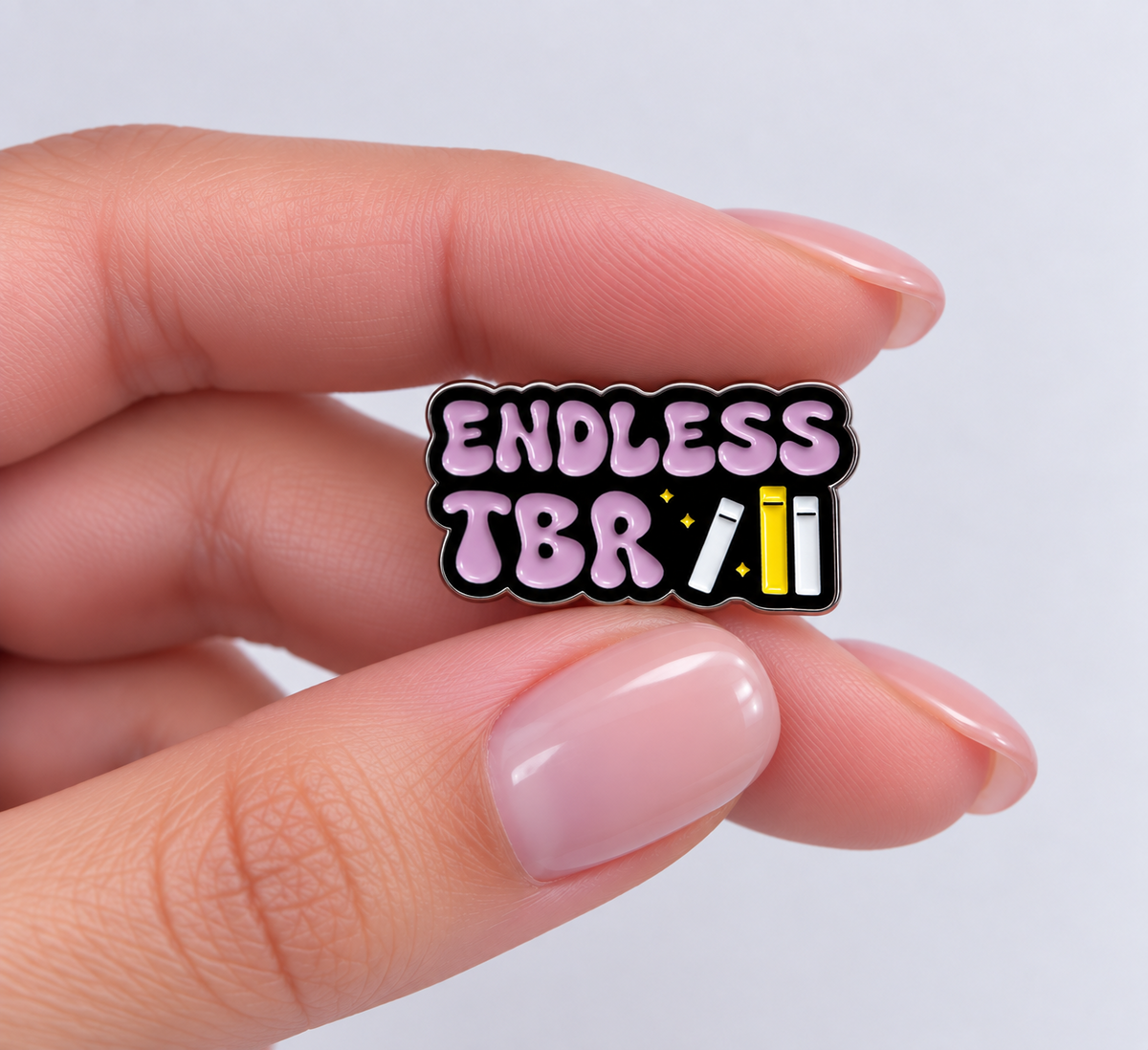 Endless TBR enamel pin held in hand to show its size