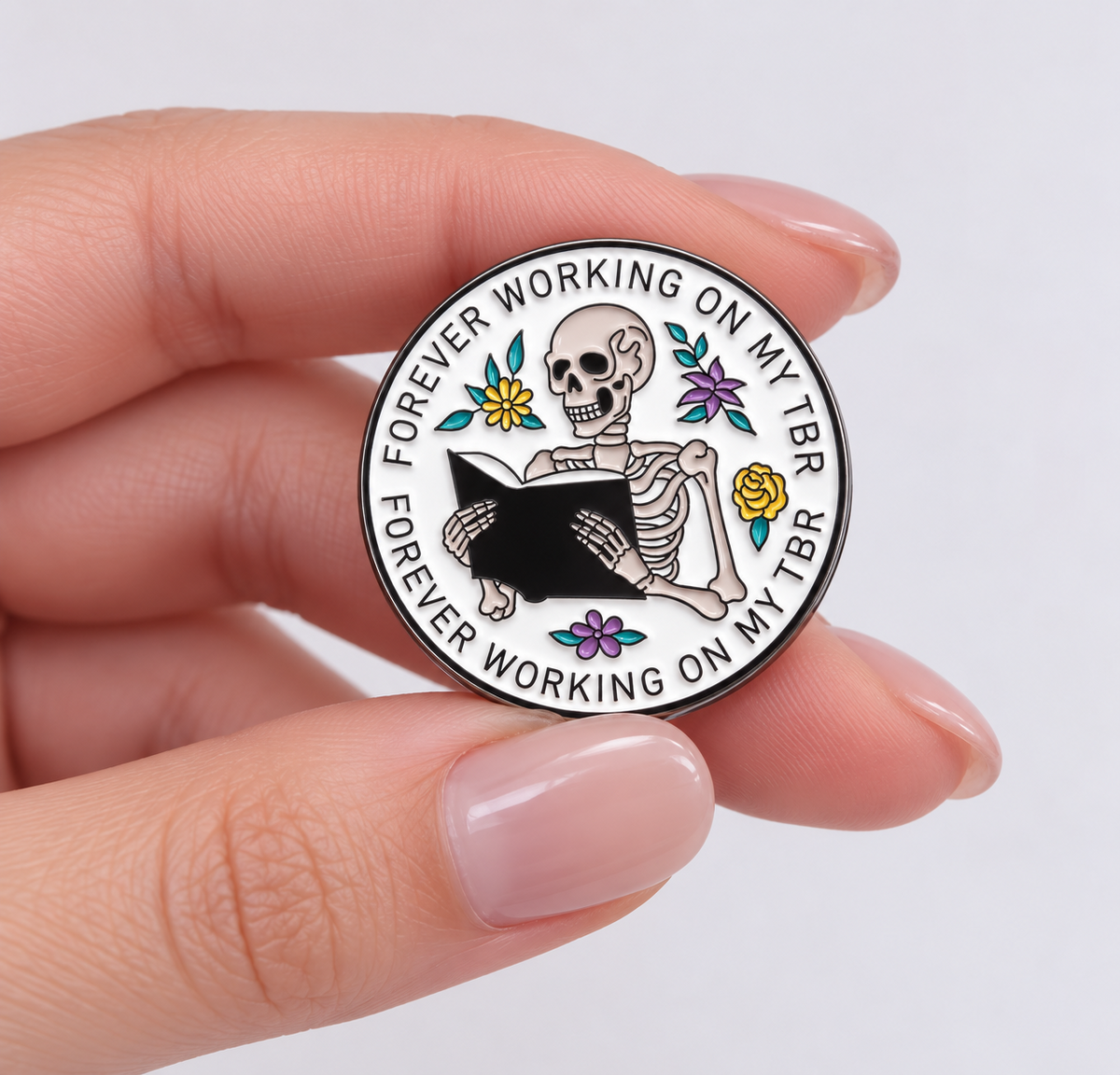 Forever Working on My TBR skeleton enamel pin held in hand to show its size