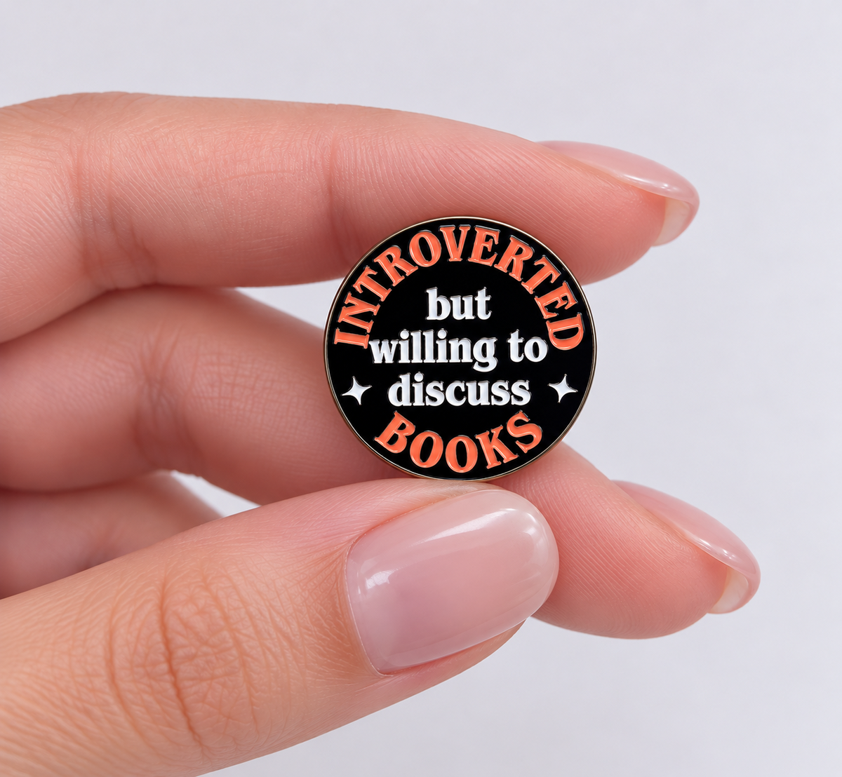 Introverted But Willing to Discuss Books enamel pin held in hand to show its size